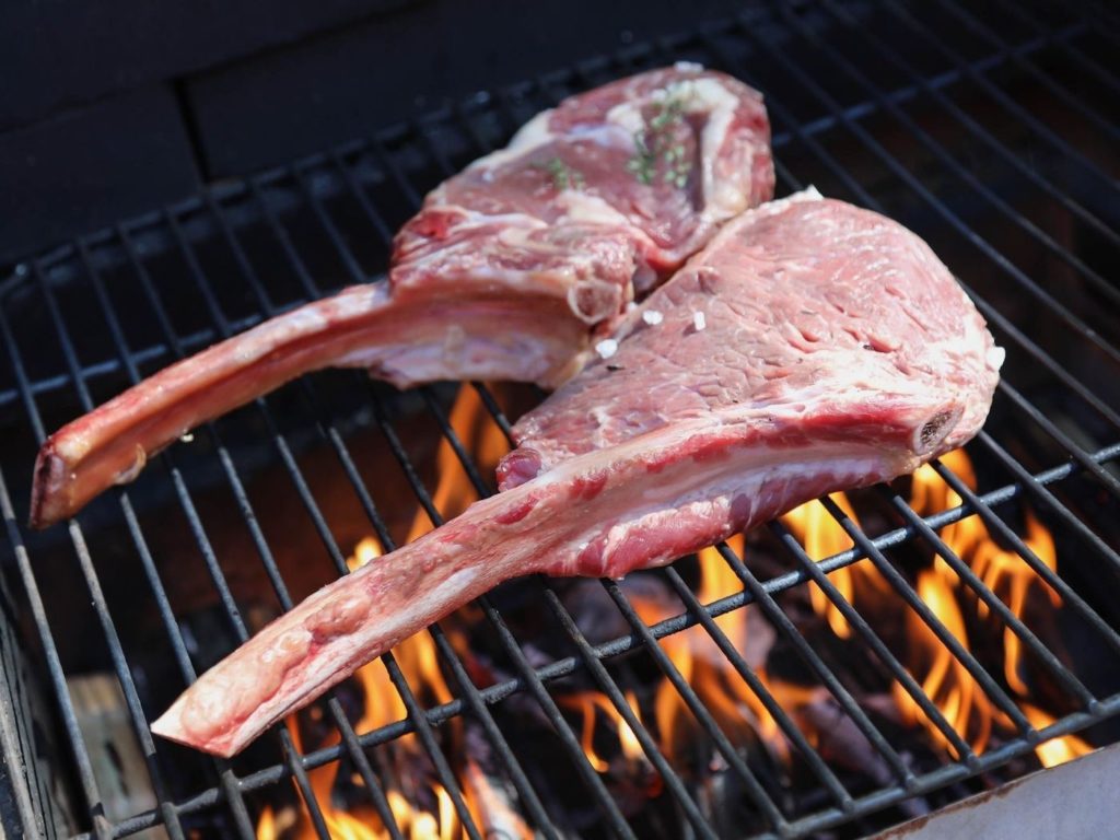 Tomahawk steaks sizzling over a charcoal BBQ